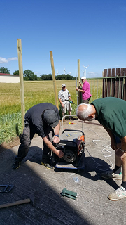 Vier Männer arbeiten bei Sonnenschein am Feldrand an neuen Holzpfosten für den Zaun.