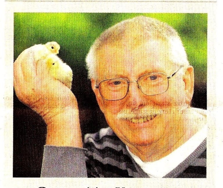 Ein älterer Mann mit Brille und Schnurrbart hält lächelnd zwei gelbe Küken in der Hand hoch, Zeitungsfoto.